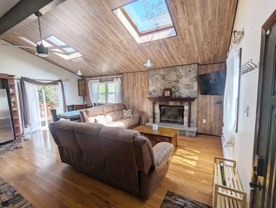 Living room seen from the entrance: sectional sofa facing the stone fireplace and TV, skylights in the vaulted ceiling